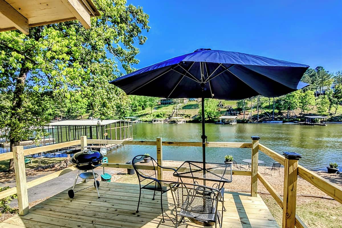 A wooden deck with outdoor furniture, a grill, and a view of a lake.