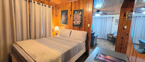 Una habitación con paneles de madera, una cama, una mesa con un libro y una lámpara.