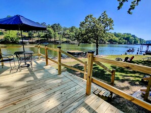 A wooden deck with a railing overlooking a lake, featuring tables and chairs, and a large umbrella.