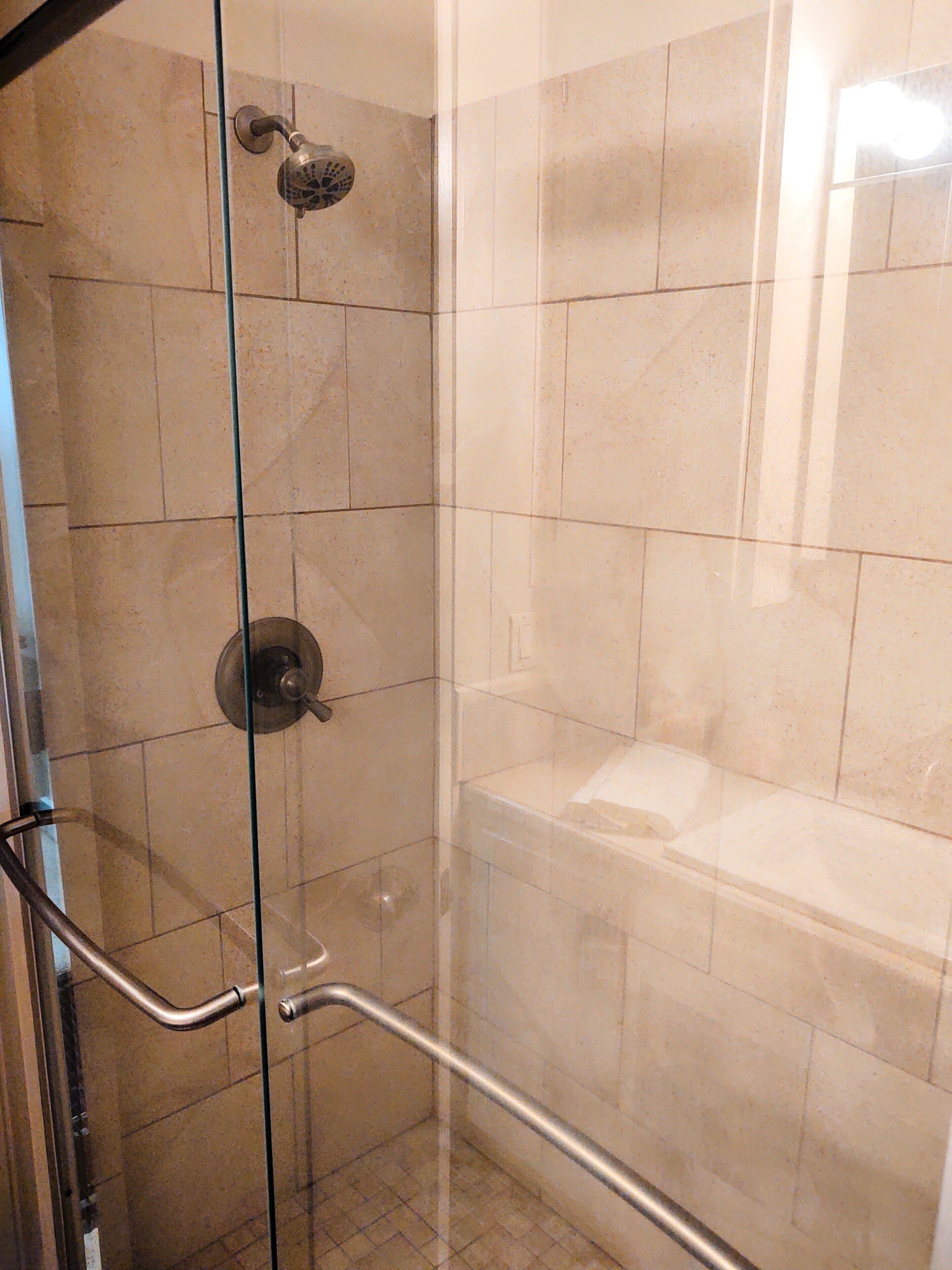 A glass-enclosed shower stall with a handheld showerhead and a handheld shower control.