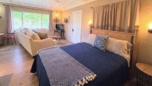 Ein Schlafzimmer mit Bett, Sofa, Deckenventilator, Fernseher und einem Fenster mit Vorhängen.