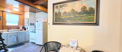 A kitchen with wooden cabinets, a microwave, a refrigerator, and a sink. There is a painting of a landscape on the wall.