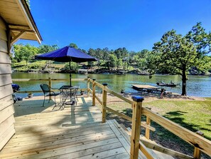 A wooden deck with outdoor furniture, a blue umbrella, and a view of a lake with boats. - Edgewater Resort (Hot Springs)