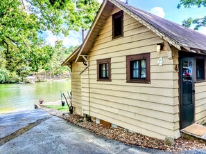A wooden cabin with a number '4' on the door, a dock, and a lake in the background.