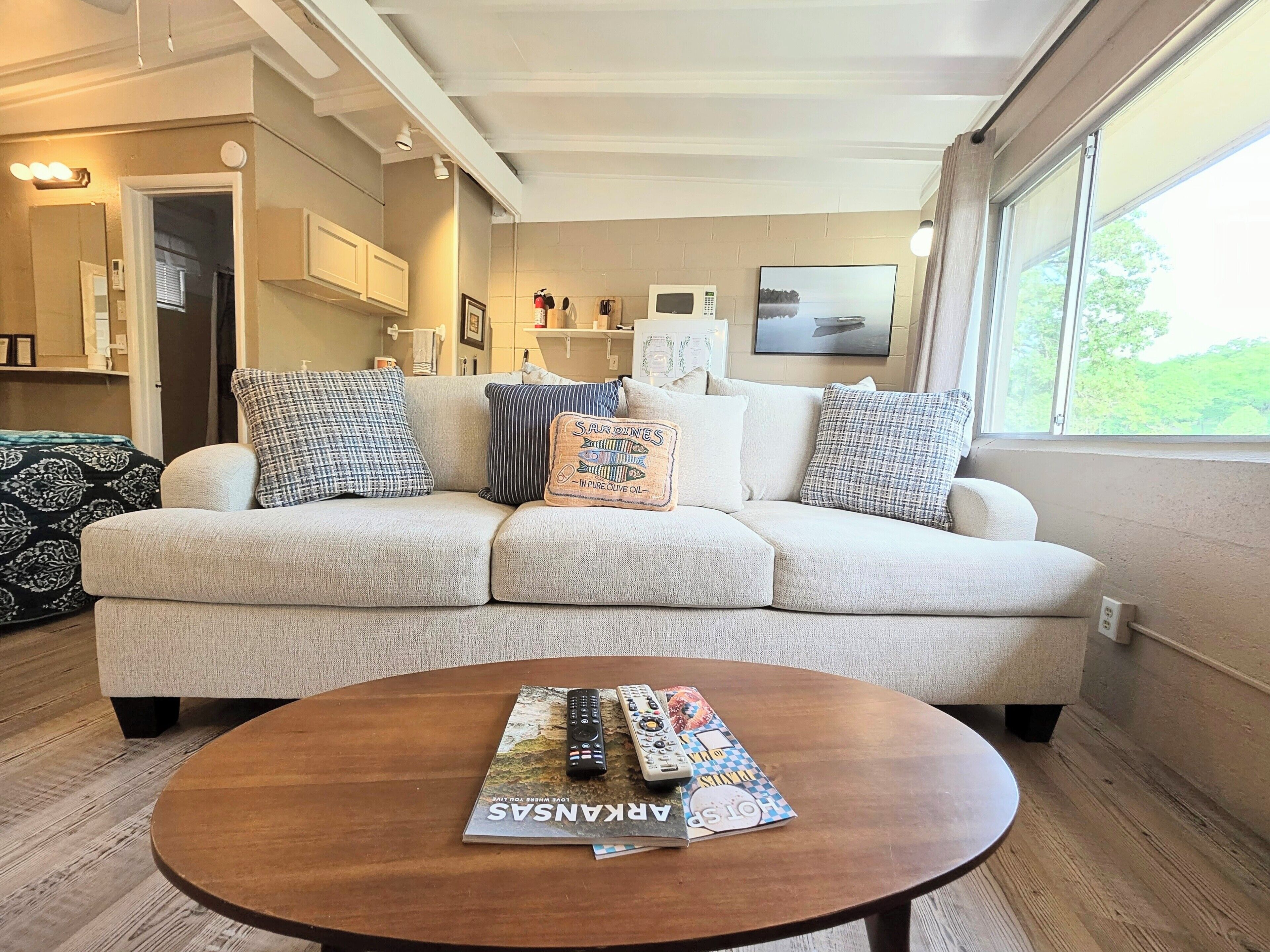 A living room with a sofa, a coffee table with magazines, a microwave, and a window with a view.