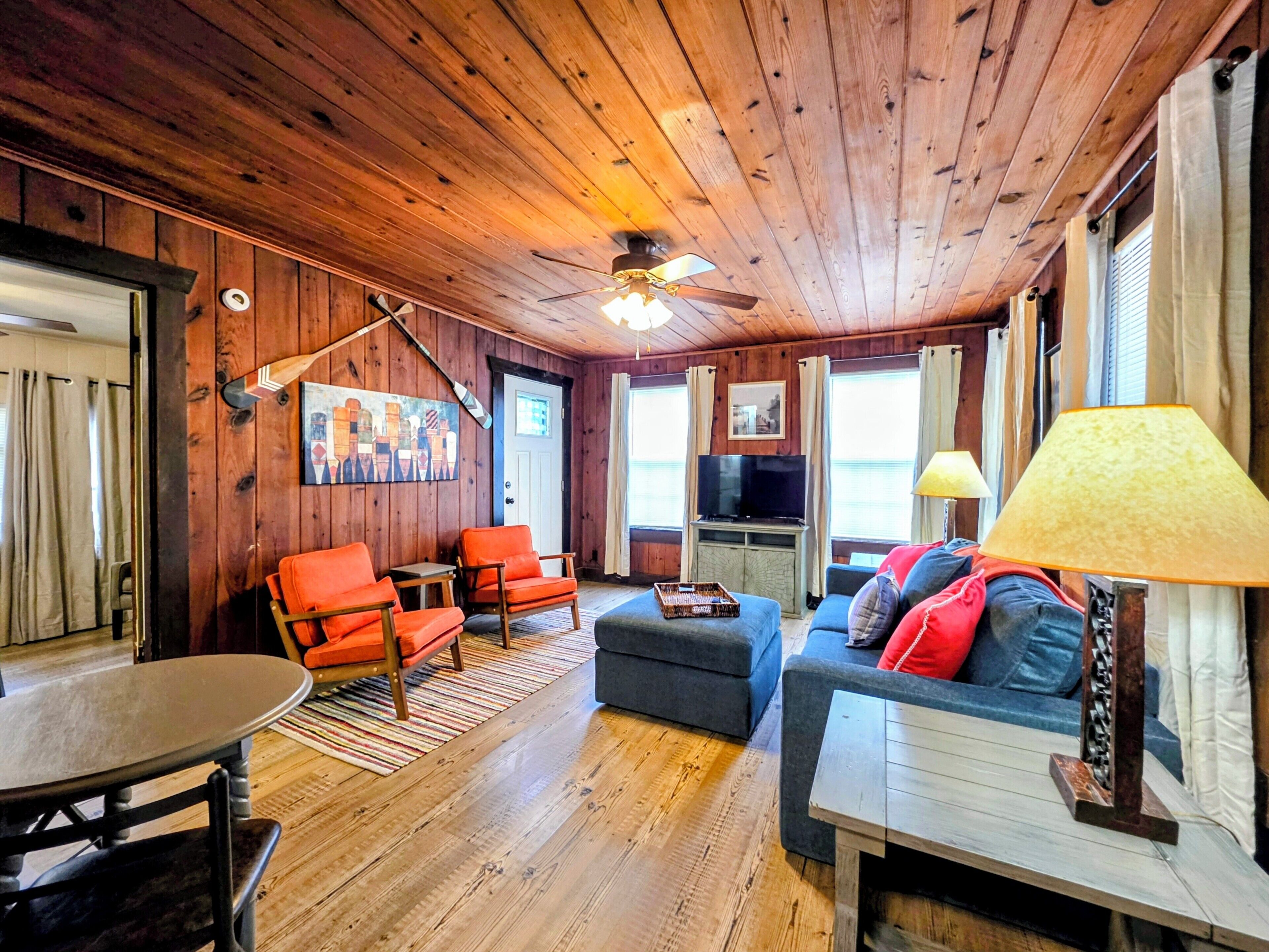 A wooden interior with a ceiling fan, a television, and a sofa with cushions.