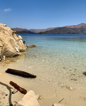 Un lago transparente con una costa rocosa y montañas al fondo.