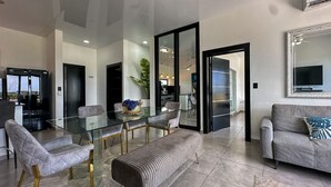 A modern living room with a glass dining table, grey sofas, and a large mirror.