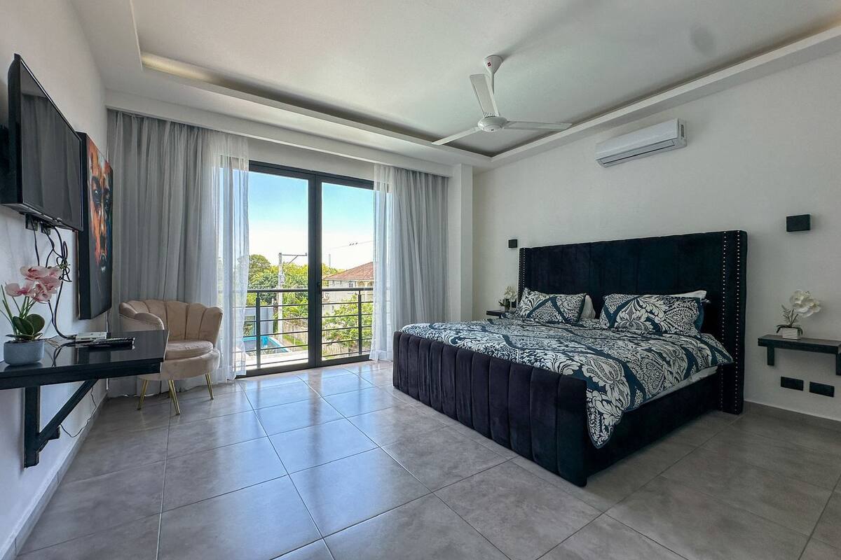 A modern bedroom with a large bed, a desk, a chair, and a balcony with a view.
