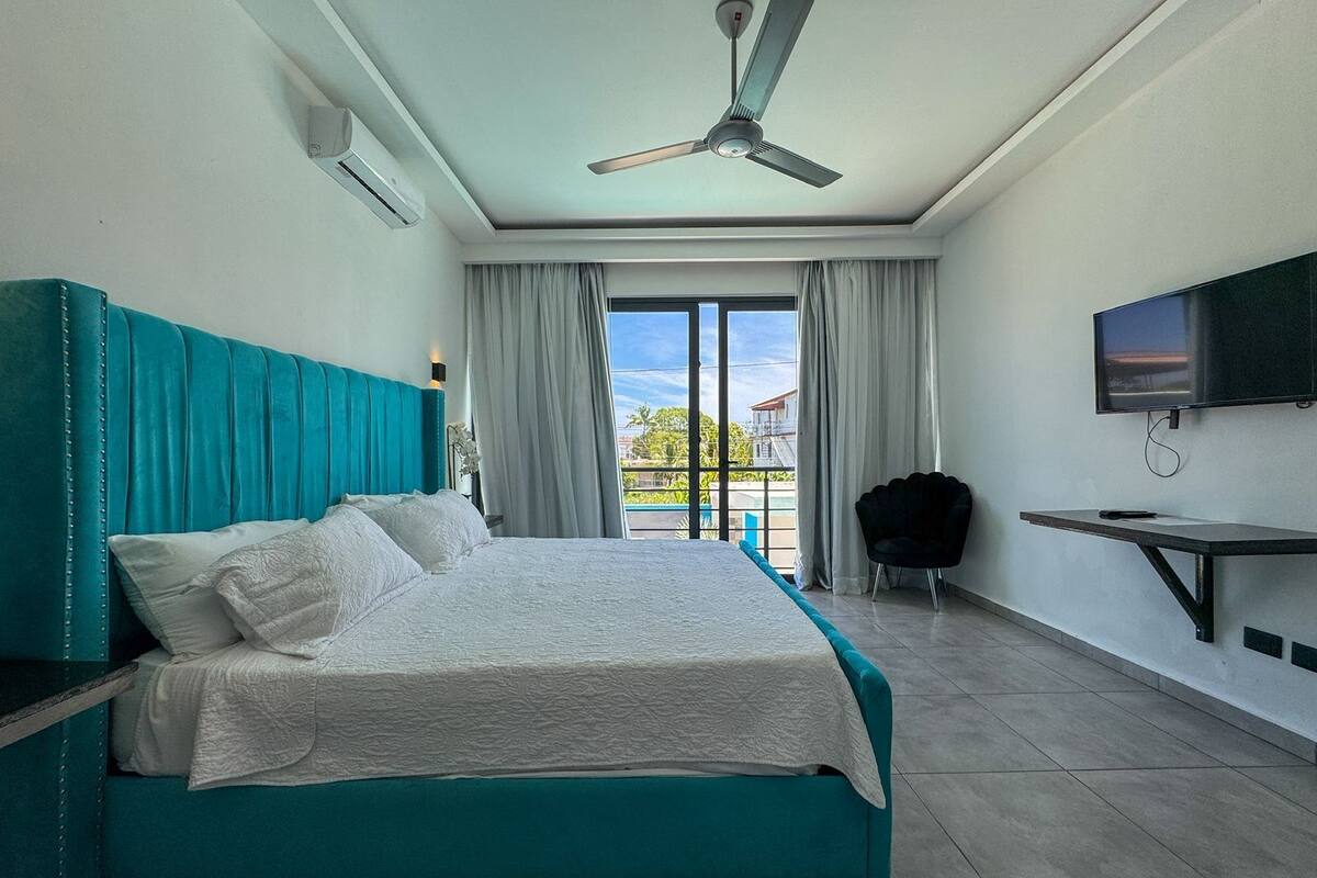 A modern hotel room with a large bed, a ceiling fan, a TV, and a balcony with curtains.