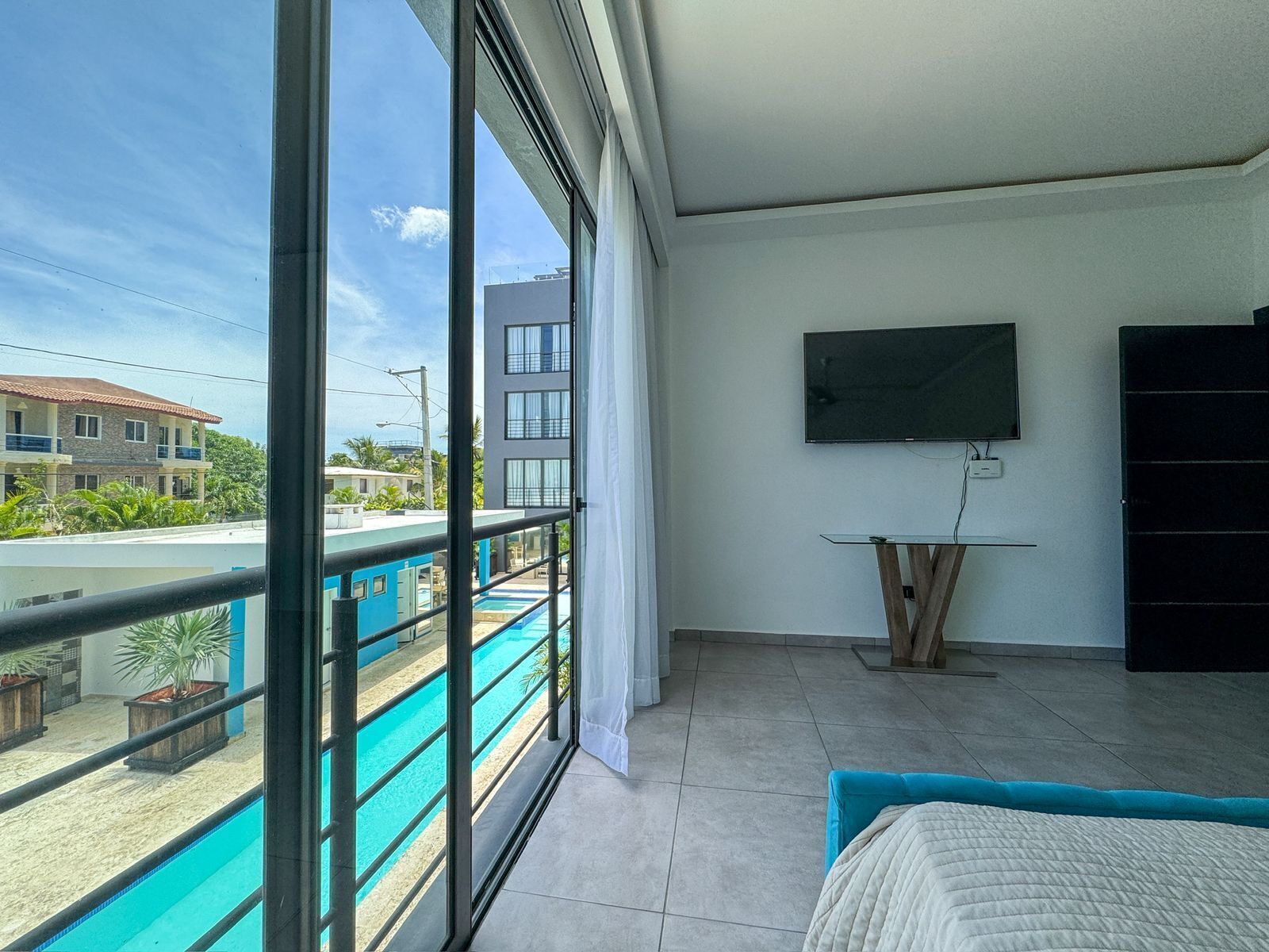 Un dormitorio moderno con un ventanal grande, televisor y balcón con piscina.