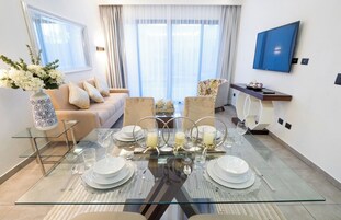 Un comedor con una mesa de vidrio dispuesta para cuatro personas, rodeado de sofás y un televisor montado en la pared.