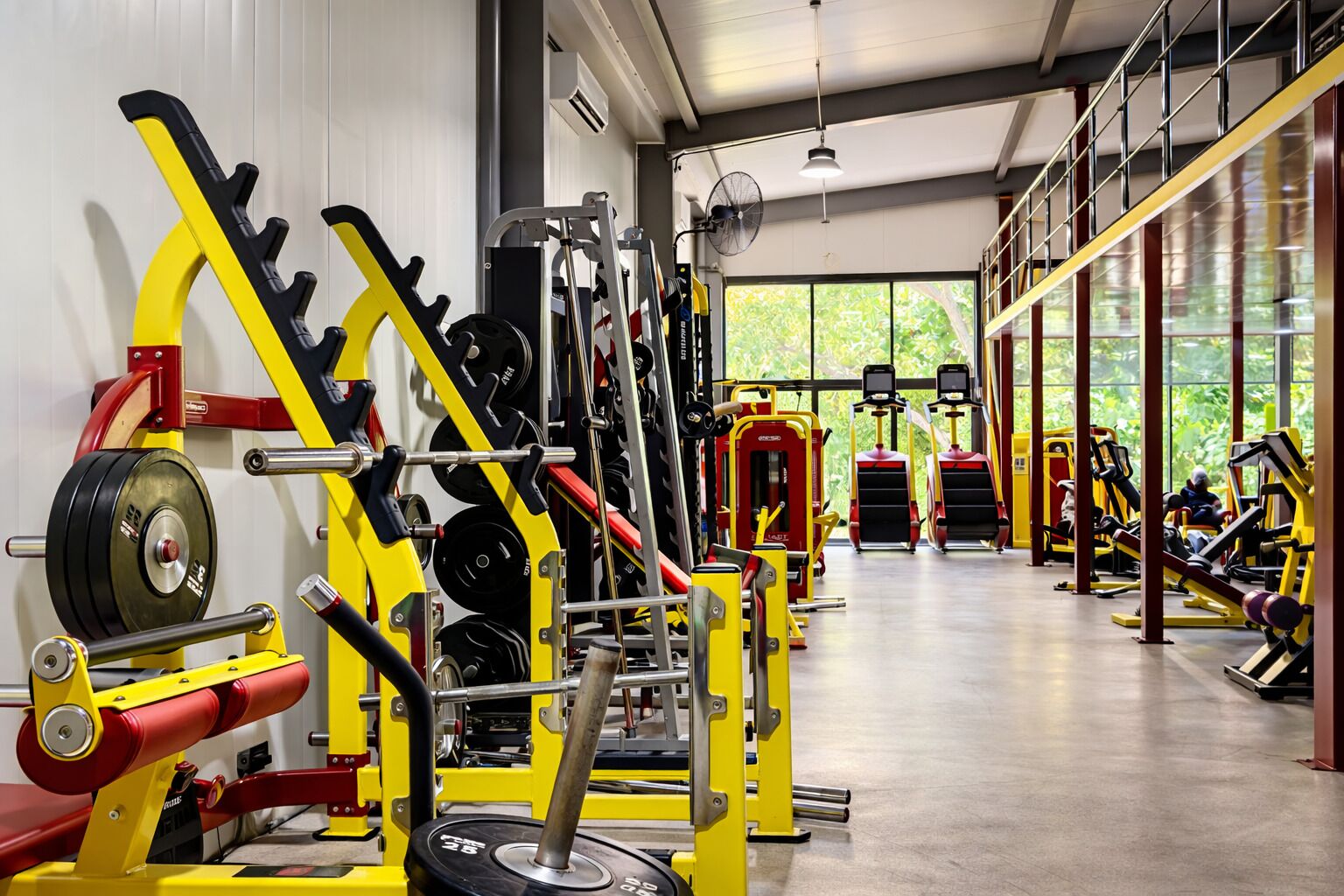 A gym with various weightlifting equipment, large windows, and a clean, modern interior.