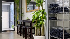 A hotel room with a desk, chairs, a mirror, a potted plant, and a metal rack with towels.