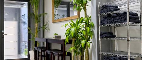 Habitación de hotel con escritorio, sillas, un espejo, una planta en maceta y un perchero con toallas.