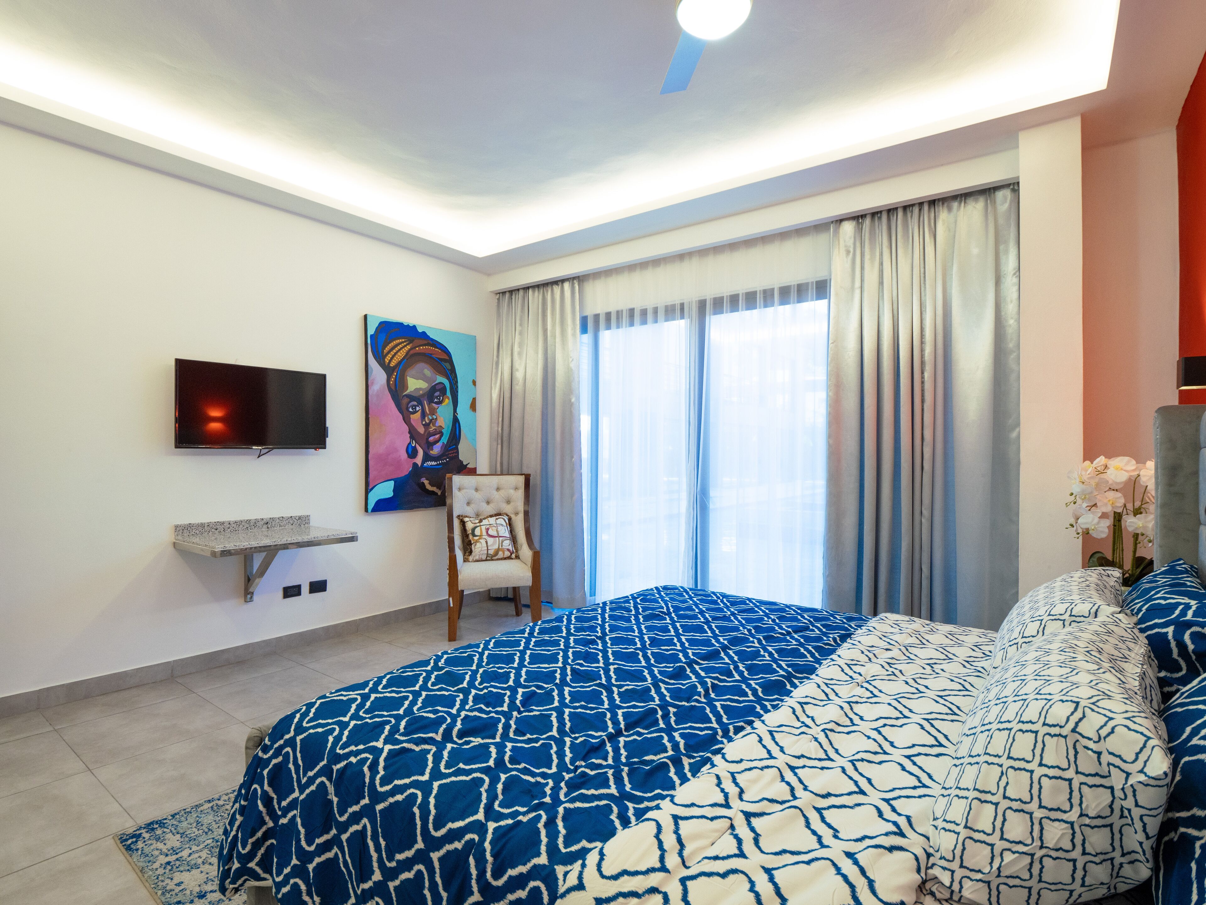 A modern bedroom with a large bed, a TV mounted on the wall, and a painting.