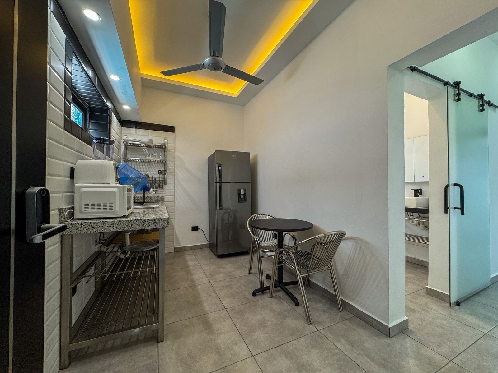 Cocina compacta con microondas, refrigerador y comedor con sillas.
