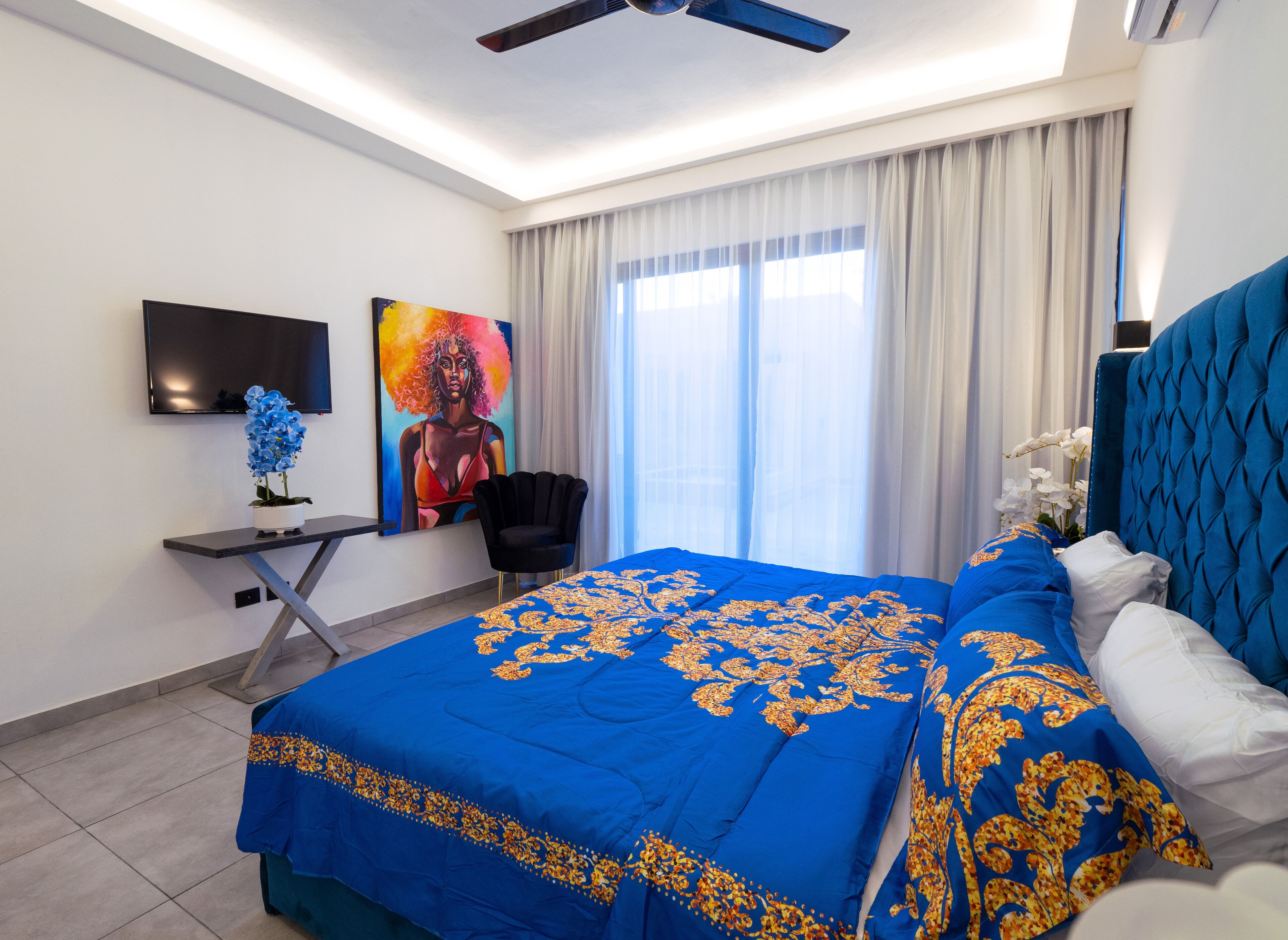 Une chambre d’hôtel avec un grand lit, un bureau, une chaise, une télévision et un ventilateur de plafond.