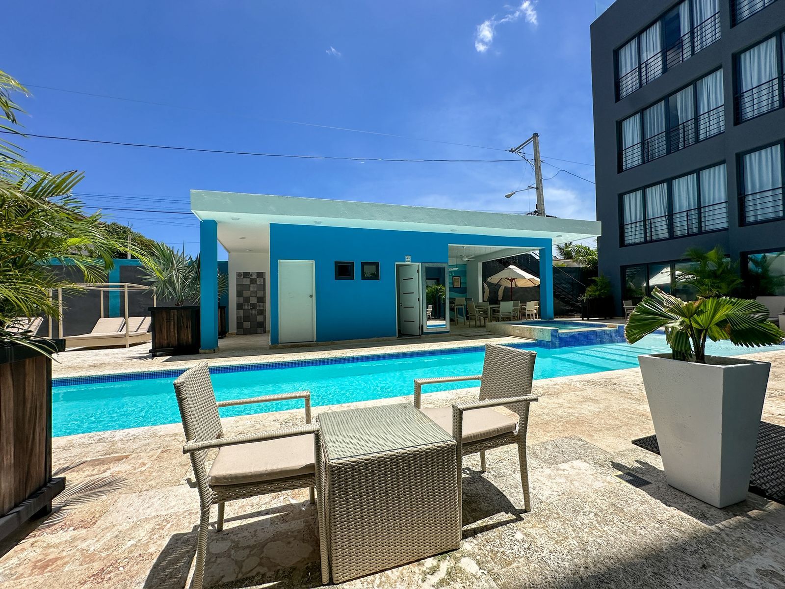 A modern building with a pool, outdoor seating, and a clear blue sky.
