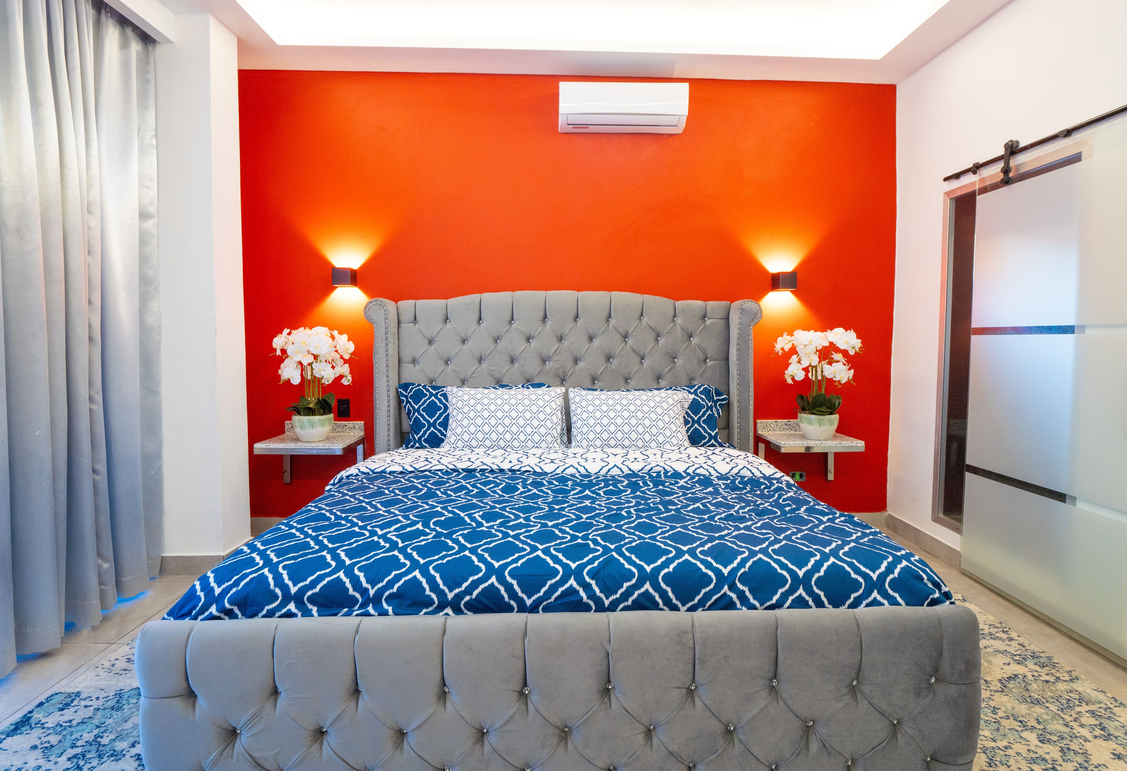 Une chambre avec un grand lit, deux tables de chevet avec des lampes et un mur d’accent rouge.