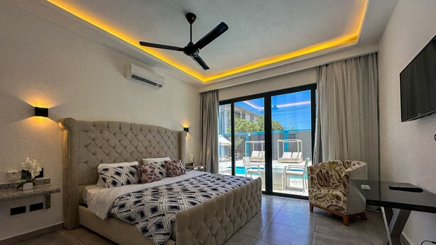 A modern bedroom with a large bed, a ceiling fan, and a view of a pool and outdoor seating.
