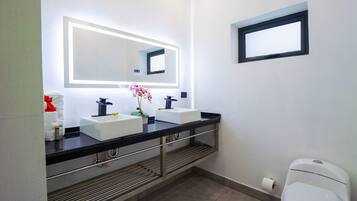 A modern bathroom with two sinks, a large mirror, and a toilet.