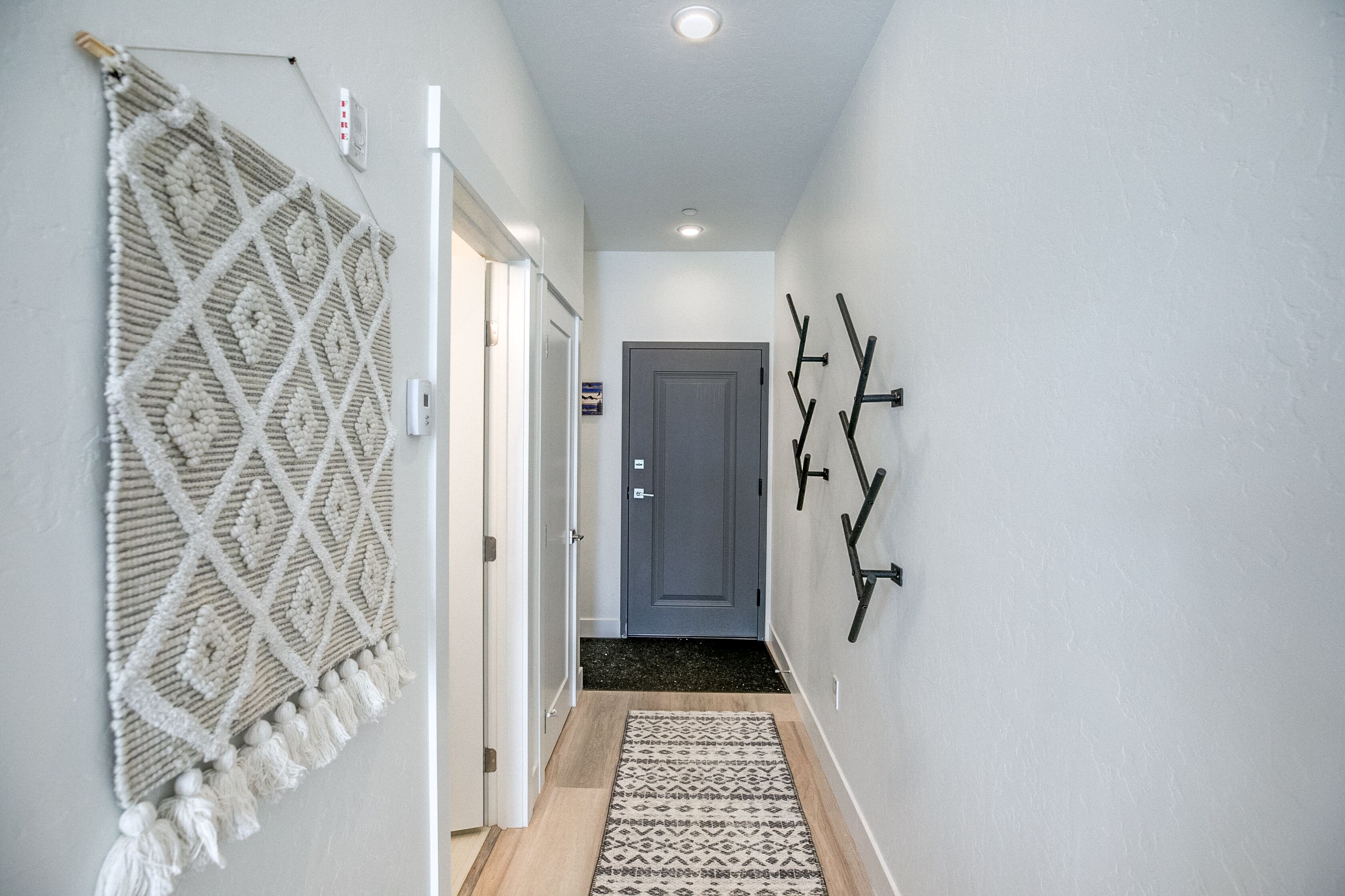 A hallway with a macramé wall hanging, a patterned rug, and wall-mounted hooks.