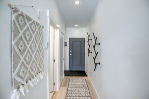 Een gang met een macramé wanddecoratie, een patroonrijk vloerkleed en wandhaken.