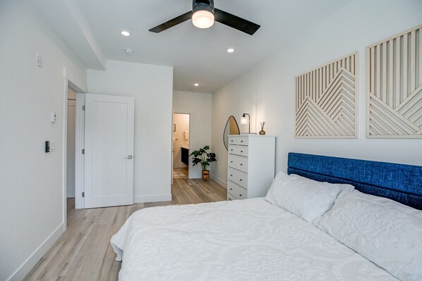 A bedroom with a bed, a dresser, a ceiling fan, and a wall with geometric decor.