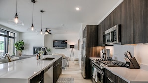 A modern kitchen with a large island, dark wood cabinets, stainless steel appliances, and pendant lighting.