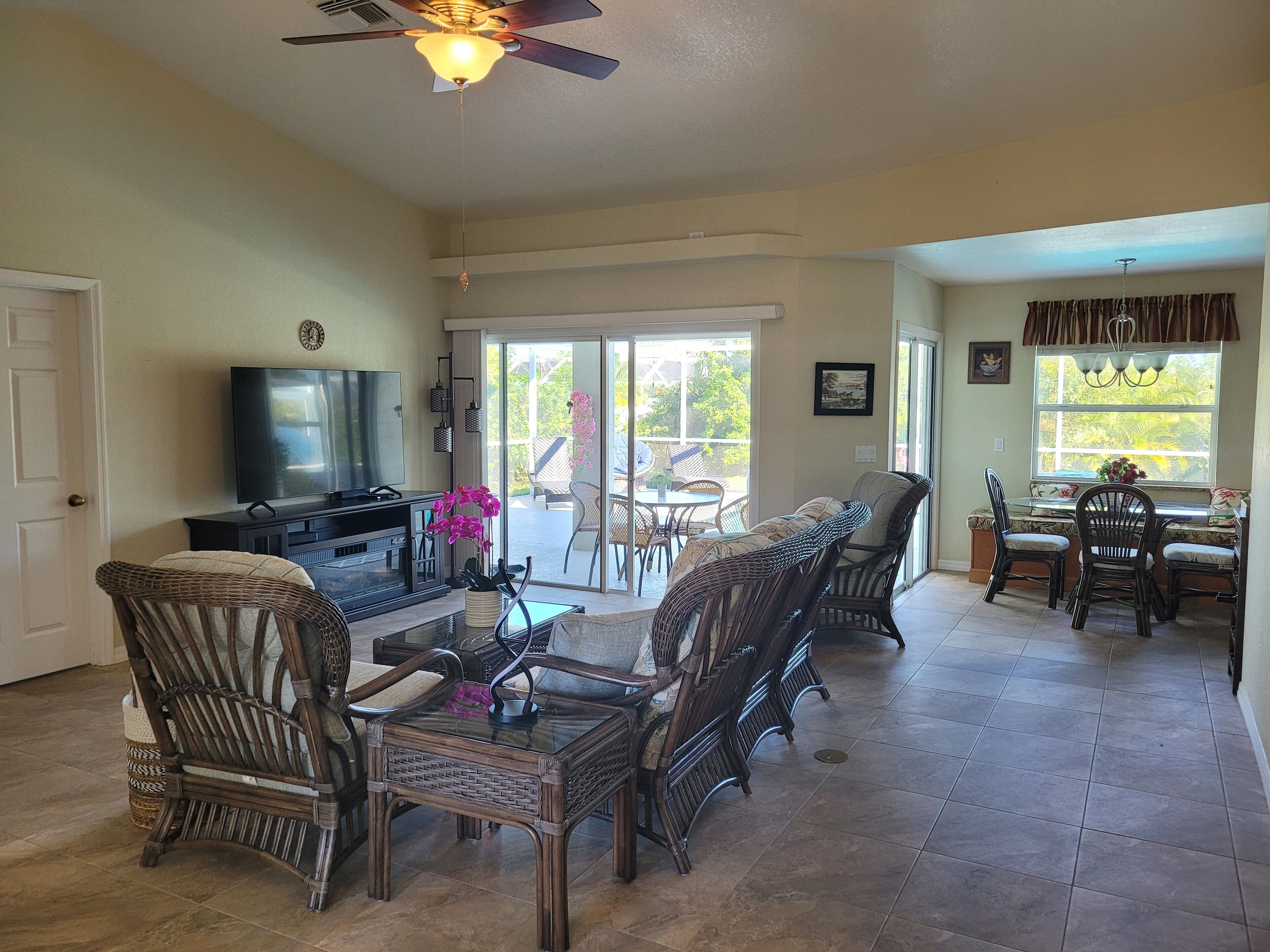 A spacious living room with a television, wicker furniture, a glass coffee table, and a ceiling fan.