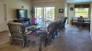 A spacious living room with a television, wicker furniture, a glass coffee table, and a ceiling fan. - 2 Bed 2 Bath Heated Pool Vacation House, Very Private (Rotonda West)