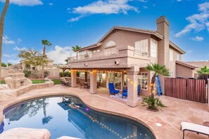 Une grande maison avec une piscine, un espace salon extérieur et une cheminée en pierre.
