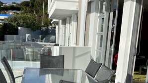 Un patio al aire libre con una mesa de vidrio y sillas de mimbre.