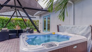 Ein Whirlpool mit Holzverkleidung, umgeben von Gartenmöbeln und einer überdachten Sitzgruppe.