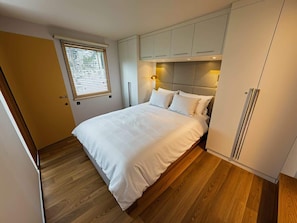 A bedroom with a bed, wooden flooring, a window, and built-in cabinets.
