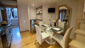 A modern dining area with a glass table, white chairs, a flat-screen TV, and a wooden staircase. - Fulham 2-Bed | Both En-Suite | Private Patio | Sleeps 5 (London)