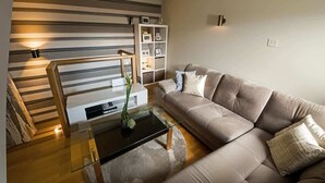 A modern living room with a sofa, a glass coffee table, a bookshelf, and a staircase. - Fulham 2-Bed | Both En-Suite | Private Patio | Sleeps 5 (London)