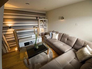 Una sala de estar moderna con un sofá, una mesa de centro de vidrio, una estantería y una escalera.