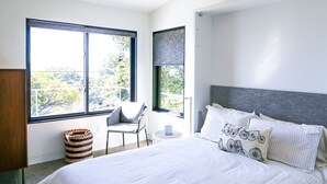 Een moderne slaapkamer met een groot bed, een stoel en een raam met uitzicht op bomen.