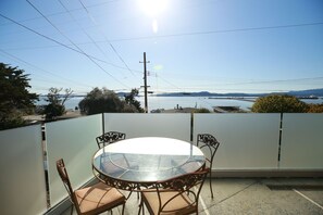 A round glass table with four chairs on a balcony overlooking a body of water and distant land.