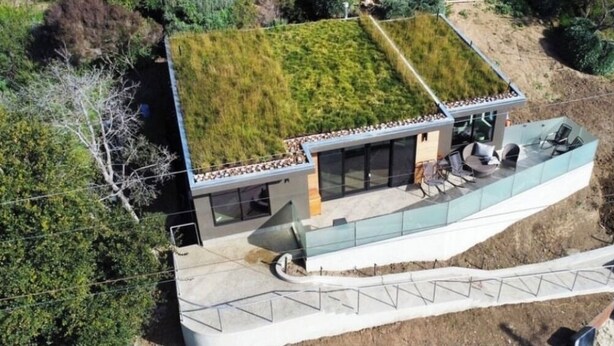 Een modern huis met een groen dak, een glazen conservatorium en een terras.