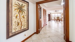 Un pasillo con un grabado botánico enmarcado en la pared, una puerta de madera y un suelo de baldosas que conduce a un comedor.