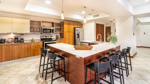Una cocina moderna con armarios de madera, una isla grande con taburetes de bar, electrodomésticos de acero inoxidable e iluminación colgante.