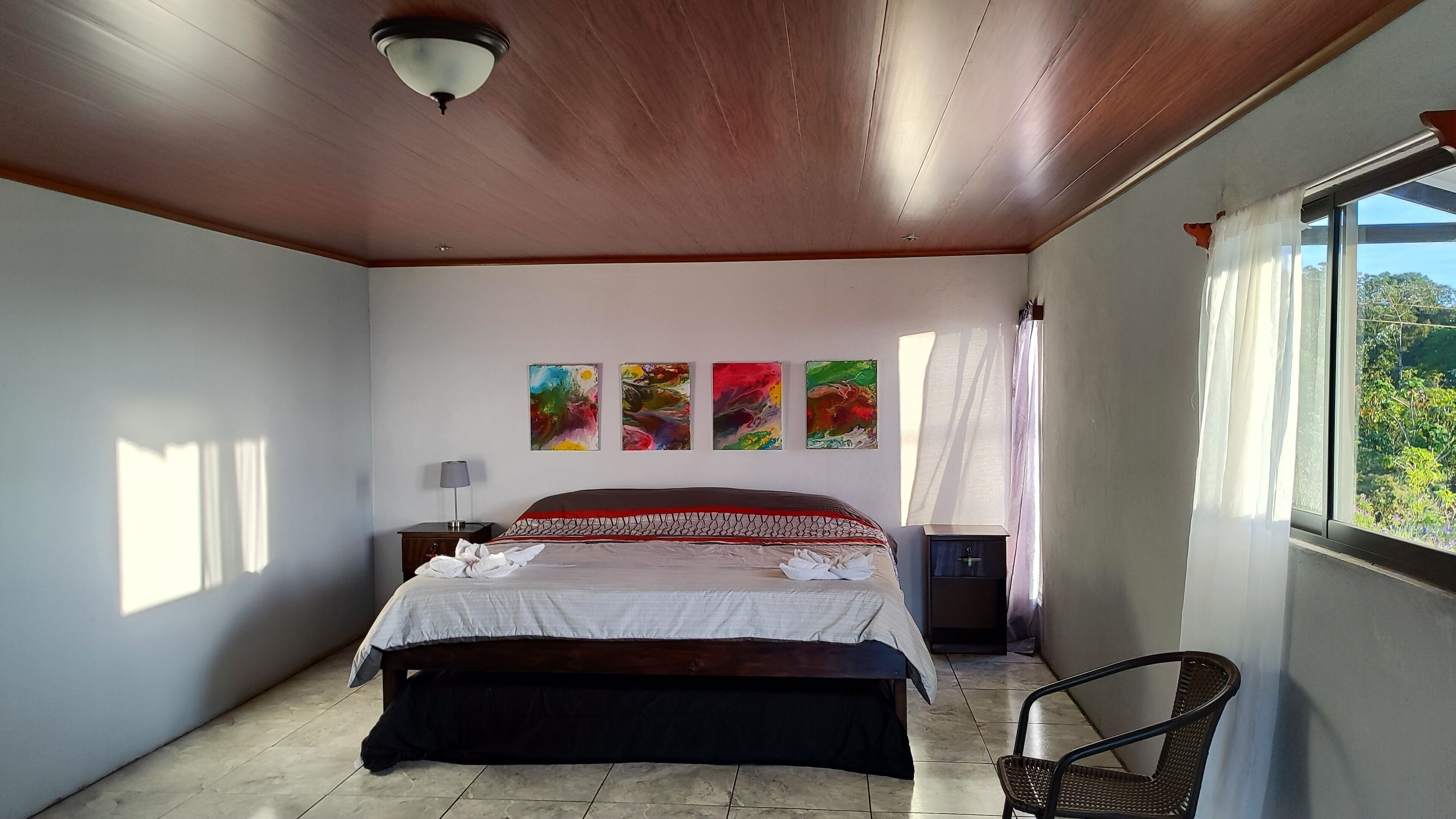 Un dormitorio con cama, mesita de noche, una silla y ventana con vistas.