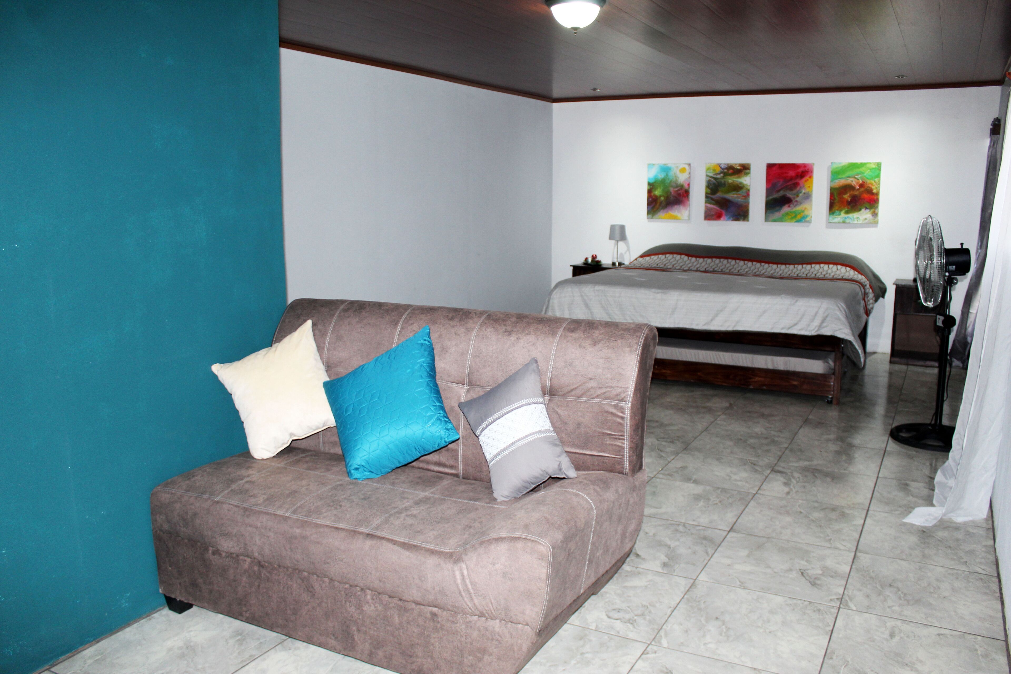 Ein Schlafzimmer mit einem Bett, einem Schlafsofa und einem Standventilator.