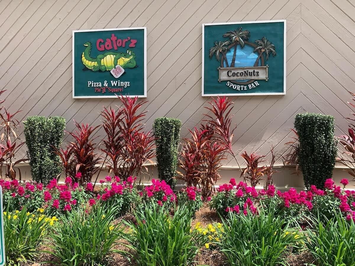 Twee restaurantschotten, 'Gatorz Pizza & Wings' en 'CocoNutz Sportz Bar', met een aangelegde tuin ervoor.