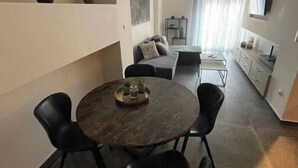 Un espace repas moderne comprenant une table ronde et quatre chaises, un canapé et un coin cuisine avec des placards et un plan de travail.