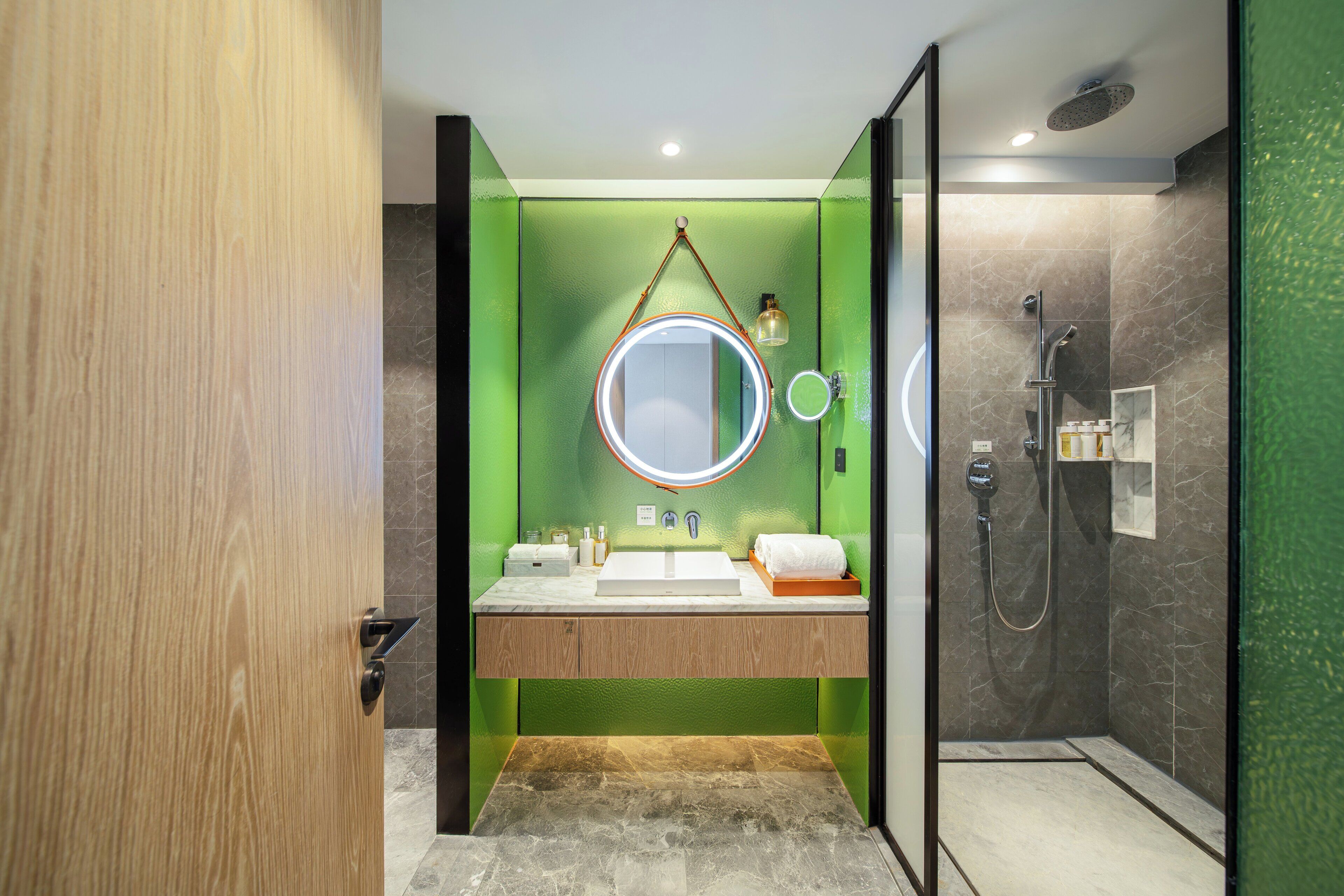 A modern bathroom with a wooden vanity, a round mirror, and a shower area.