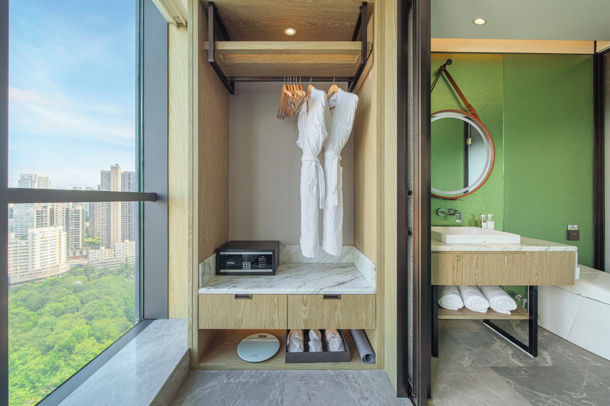 Een moderne badkamer met een groot raam, een houten wastafelmeubel, een douchegedeelte en uitzicht op de stad.